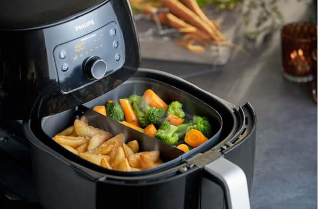 Philips Premium Airfryer XXL HD9651/91 cooking crispy fries and healthy vegetables in dual compartments.